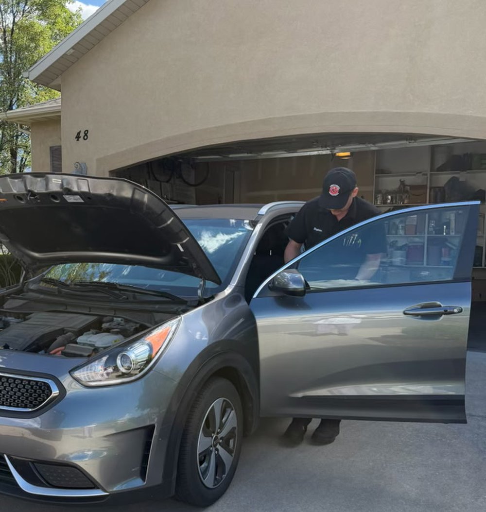 A technician working under the hood of a customer's vehicle during a mobile appointment.